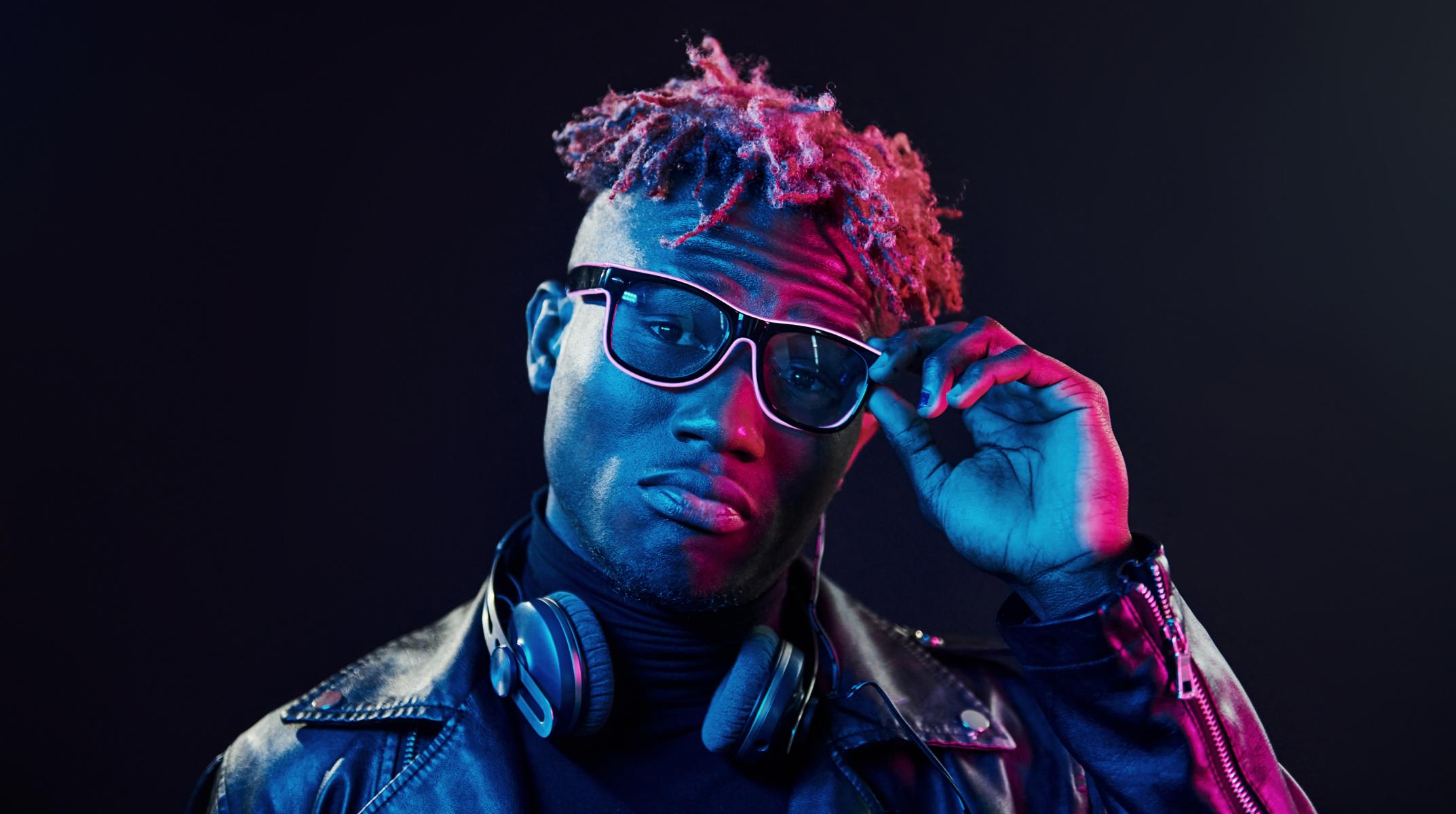 Stylish glasses and wireless headphones. Futuristic neon lighting. Young african american man in the usability studio.